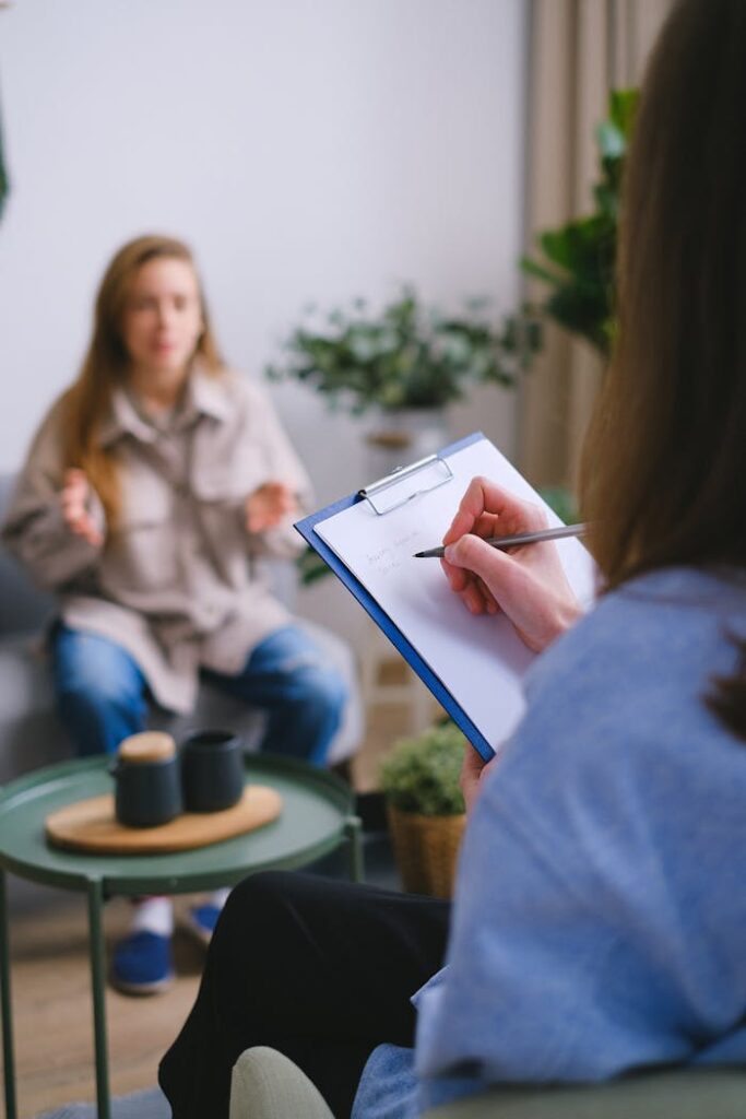 crop-psychologist-writing-on-clipboard-during-psychotherapy-session-7176036 Unrecognizable female psychologist taking notes on clipboard while listening to patient sitting on blurred background during psychotherapy consultation in office